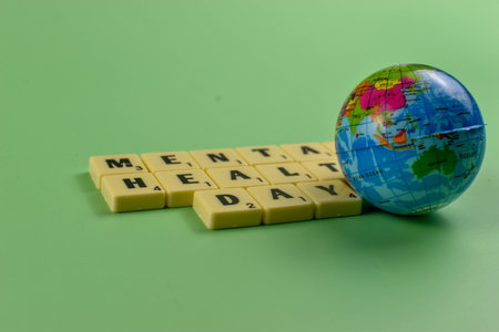 Scrabble tiles spell Mental Health Day beside globe, symbolizing global recognition of emotional well-being and mental health awareness.の写真素材