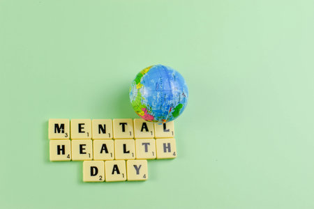 Scrabble tiles spell Mental Health Day beside globe, symbolizing global recognition of emotional well-being and mental health awareness.の写真素材