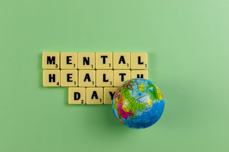 Scrabble tiles spell Mental Health Day beside globe, symbolizing global recognition of emotional well-being and mental health awareness.の写真素材
