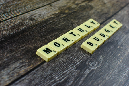 Scrabble tiles spell Monthly Budget diagonally on wood, representing routine financial planning and expense tracking over a monthly cycle.の写真素材