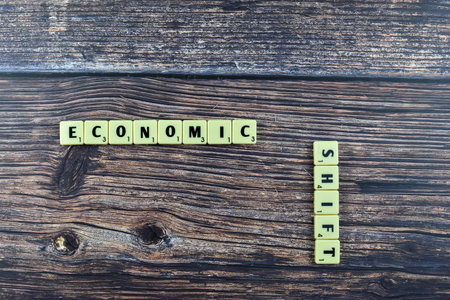 Scrabble tiles spell Economic Shift on wood, symbolizing transformation in financial systems or market conditions through intersecting wordplay.の写真素材