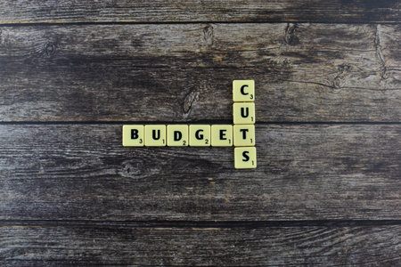 Scrabble tiles spell Budget Cuts on wood, symbolizing financial reductions often implemented in government or organizational spending strategies.の写真素材