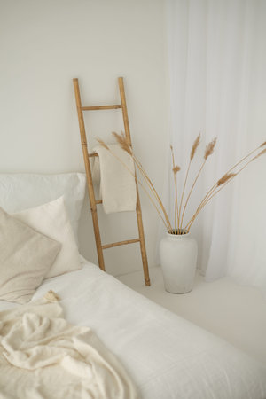 Modern bedroom interior with white pillows, wooden ladder and dried flowers in vaseの写真素材