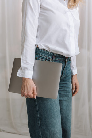 cropped view of businesswoman in white blouse and jeans holding laptopの写真素材