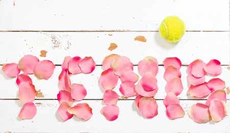 Photo of a tennis ball on a text written in rose petals whose written content is tennis.The photo is an overhead shot in horizontal format on a white wooden background.の写真素材