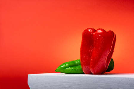Photograph of a red pepper and a green Italian pepper on a white wood and red background.の写真素材
