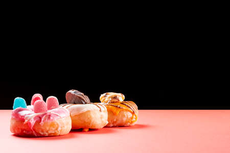 Photograph of three donuts decorated with chocolate cookies and jelly beans on a red card and a black background.の写真素材