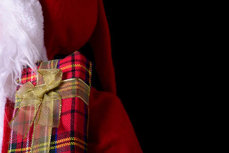Close-up of a red gift package with a gold bow on the Santa Claus props. The photograph has a copy space, a black background and can be used for a Christmas postcard.の写真素材