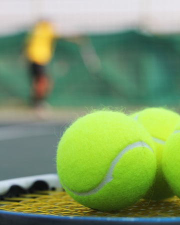 Tennis balls on racket strings with a sports person practising in the backgroundの写真素材