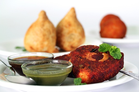 Indian deep fried snack cutlet made of potatoes, masala and cashew with chutneys and another popular snack samosa in the backgroundの写真素材