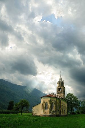 Old church on the background of mountains and contrasting sky with sunbeamsの写真素材