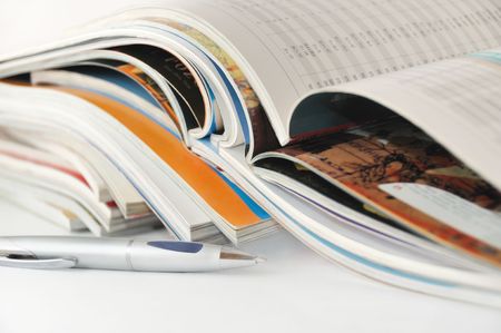 A pile of magazines, upper ones opened, and a penの写真素材