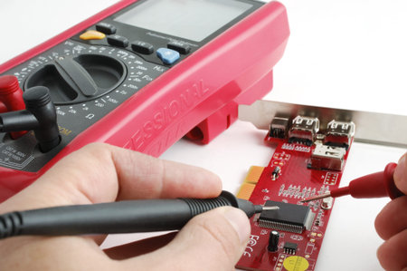 Computer technician examining a circuit board by a professional multimeter