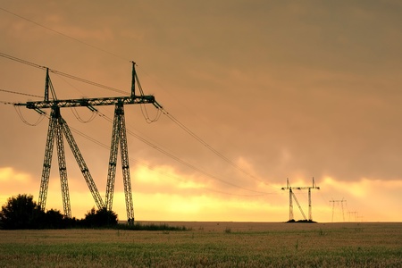 Electric power line in the cultivated field against vivid sunset skyの写真素材