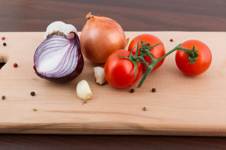 Tomatoes, garlic and onion on a board on the tableの写真素材