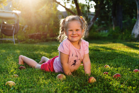 Smiling adorable little girl lying on green grass with apples aroundの写真素材