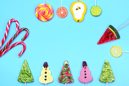 Bright colorful creative layout for Christmas, New Year and winter holidays. Candy lollipops of funny snowman, Christmas tree, fruits, and candy cane. Place for the greeting text.の写真素材