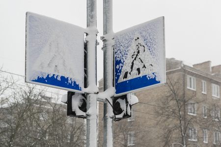 Road signs and traffic lights covered by snow during heavy snowfall in winter townの写真素材