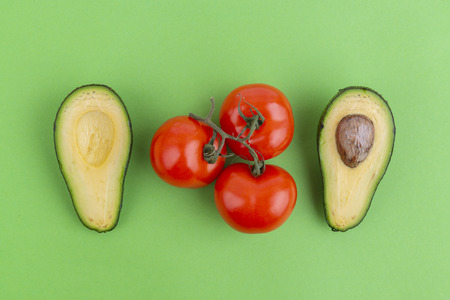 Cut avocado and tomatoes on green background. Healthy meal ingredients.の写真素材