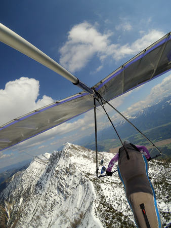 Brave pilot fly over mountain peak cobered by snow on a hang glider. Extreme aerial sport. Hang glidingの写真素材