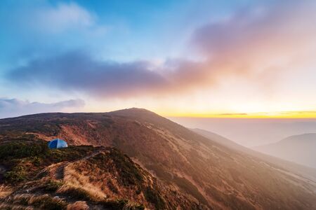 Morning at the hiking trail. Beautiful sunrise high in the Carpathian mountains with tourist tent on the mountain cliffの写真素材