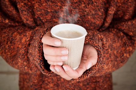 Hot drink in hands. Close up of woman hands holding a paper cup with a hot drink. Focus on hands and...