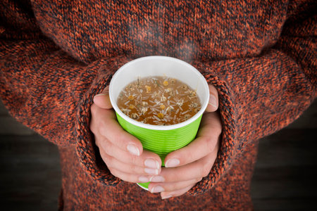 Hot tea in hands. Close up of woman hands holding a paper cup with herbal tea. Focus on hands and...