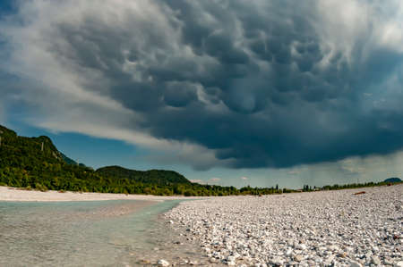 Rain cloud over Tagliamento river. Summer landscape in Northern Italy. Rare mammatus clouds and emerald riverの写真素材
