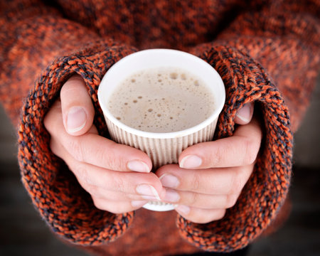 Woman hands in an oversize sweater holding a cup of coffee. Hot drink is best treat from virus...