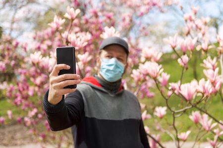 Man in medical mask making selfie with magnolia flowers during COVID-19 pandemicの写真素材