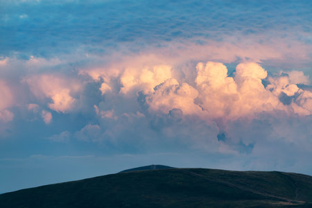 powerful thunderstorm clouds illuminated by evening sun over mountain tops