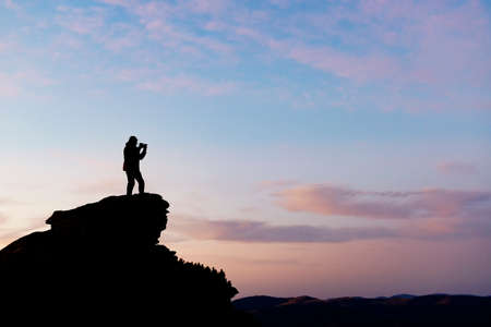 Silhouette of a wildlife photographer shooting a sunset landscape in the mountainsの写真素材
