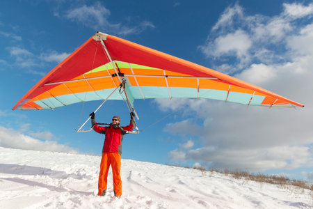 Happy man holding colorful hang glider wing on a slope. Learning to fly