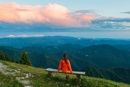 Girl on the wooden bench high in the mountains enjoy sunset. Beautiful scenery of the Soca valley,...