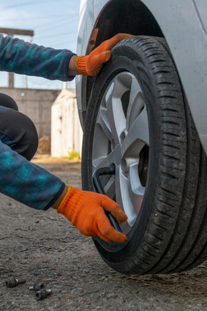 Car tire replacement. Vertical photo of driver with wrench while replacing flat tire