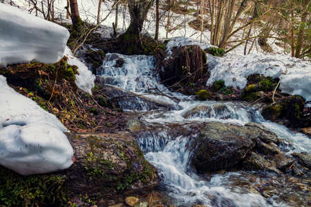 Streams of melted water in the mountains. Water balance in nature. Waterfall in the winter mountainsの写真素材