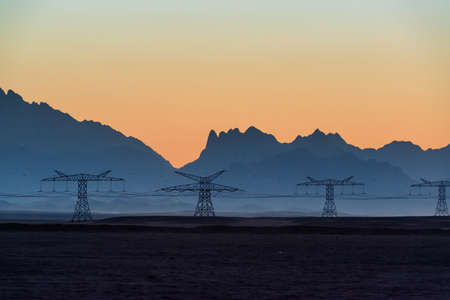 Big powerline in the desert against beautiful evening mountains silhouettesの写真素材
