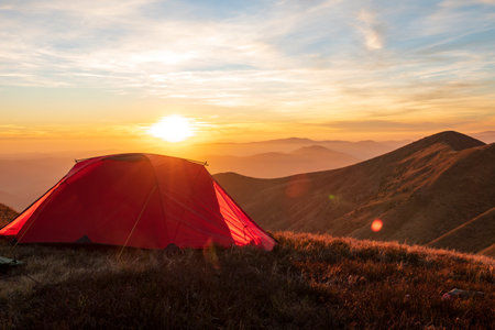 Red hiking tent on the mountain top at the sunset. Amazing outdoor vacationの写真素材