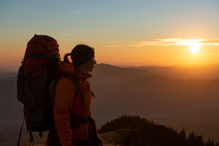 Female hiker with a backpack watching a beautiful sunset in the mountainsの写真素材