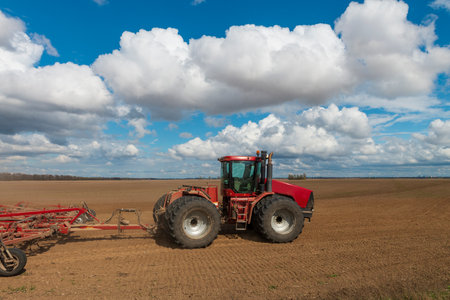Red tractor plows fresh soil in a sunny spring day. Seasonal work on the farm field. Vibrant countryside landscapeの写真素材