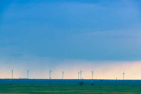 Minimalistic landscape with wind turbines and green wheat field under the rainy skyの写真素材