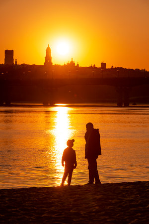 Kyiv. Ukraine, May 2023, a man with his sun enjoying the sunset on a beach in Kyiv with a beautiful view of the Pechenrsk Lavra monasteryのeditorial素材