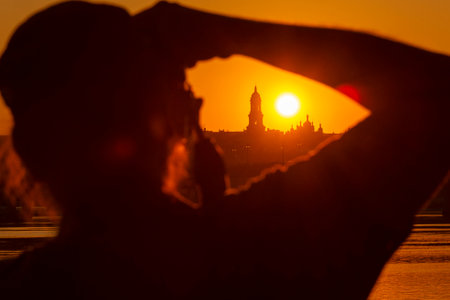 Photographer taking a photo of an amazing sunset in Kyiv. Ukraine with Lavra monastery silhouette against the setting sunの写真素材