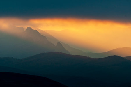 Amazing mountain landscape. Mountain peaks with dramatic low clouds and sun rays shining through the clouds.の写真素材
