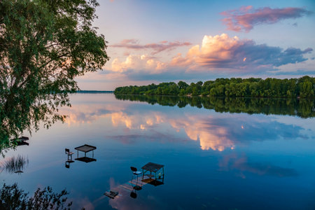 Tranquil scene on the river bank. Beautiful sunset on the river wit fishing spots and clouds reflecting in the water. Kyiv city park, Ukraineの写真素材