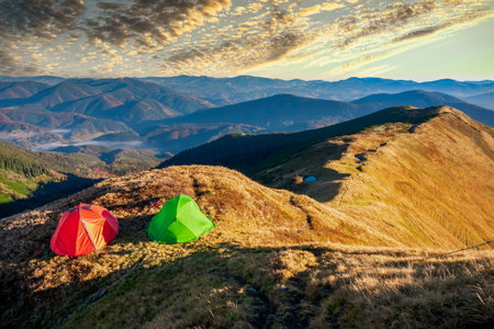 Colorful hiking tents on the mountain top at the sunset. Active vacation, hiking and exploration concept. Beauty of trekking in the mountainsの写真素材