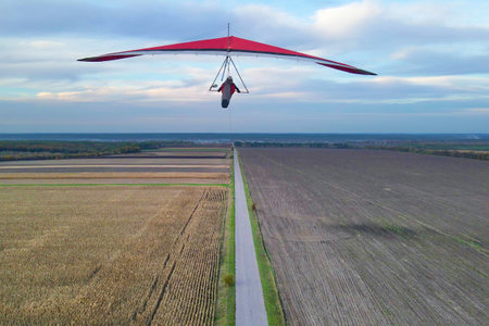 Red hang glider wing flies above the cultivated farm fields.の写真素材
