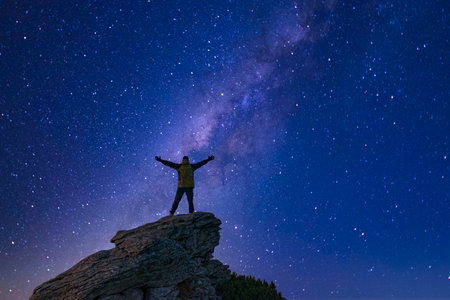 Man with raised arms looking at the night sky on the mountain topの写真素材