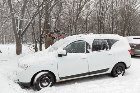 Car owner removing snow with a brush after a heavy snowfallの写真素材