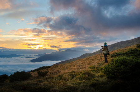 Nature travel girl photographer with tripod takes pictures of scenic landscape high in the mountains.の写真素材